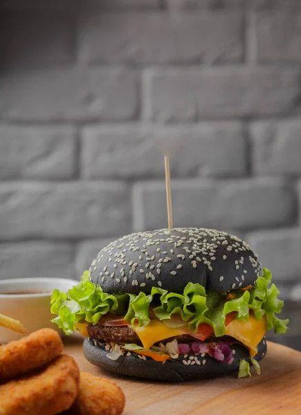 Schwarzer Burger auf Holzgrund mit Kartoffeln und Soße — Stockfoto