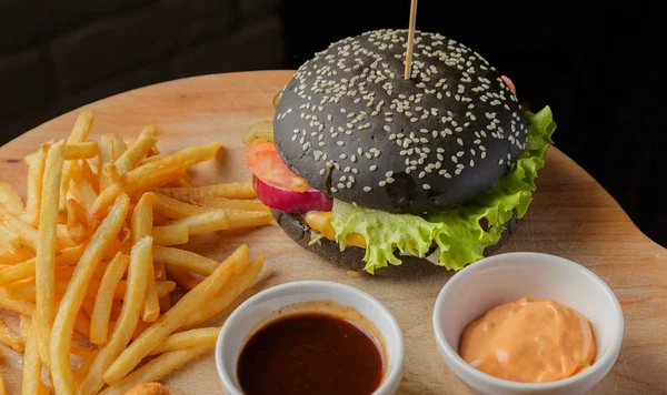 Schwarzer Burger auf Holzgrund mit Kartoffeln und Soße — Stockfoto