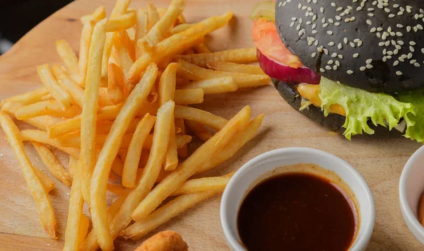 Schwarzer Burger auf Holzgrund mit Kartoffeln und Soße — Stockfoto