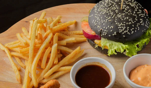 Schwarzer Burger auf Holzgrund mit Kartoffeln und Soße — Stockfoto