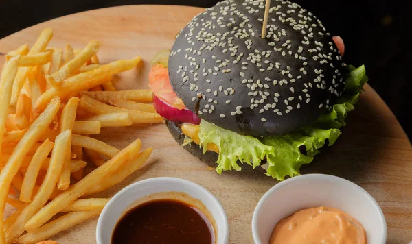 Schwarzer Burger auf Holzgrund mit Kartoffeln und Soße — Stockfoto