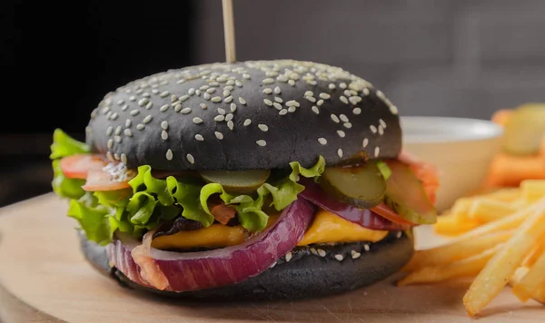 Schwarzer Burger auf Holzgrund mit Kartoffeln und Soße — Stockfoto