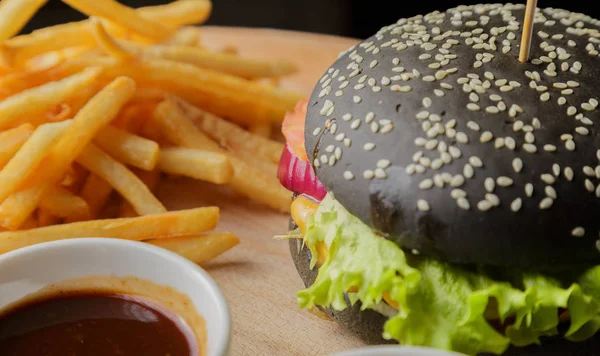 Schwarzer Burger auf Holzgrund mit Kartoffeln und Soße — Stockfoto