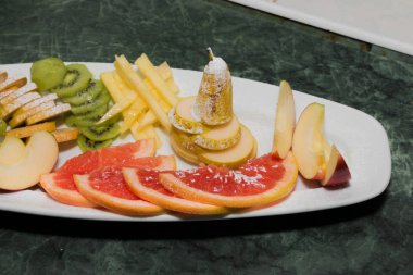 Beyaz bir tabak, üzüm, kivi, portakal, armut meyve dilimlenmiş