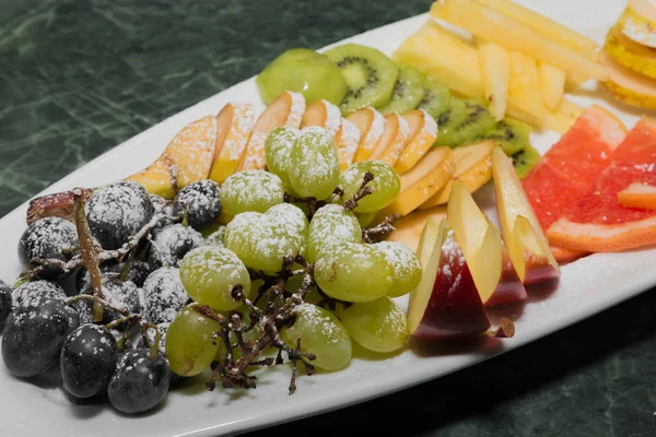 Sliced fruit on a white plate, grapes, kiwi, orange, pear — Stock Photo, Image