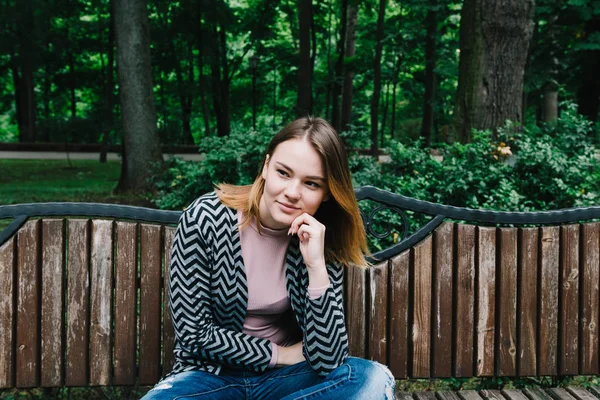 Porträt einer stilvollen Frau auf einer Holzbank im Park. — Stockfoto