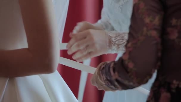 Мужчина привязывает корсет к свадебному платью невесты — стоковое видео