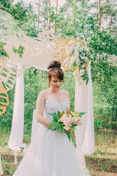 Mooie vrouw in een trouwjurk op een photozone gedecoreerd met verse bloemen, die zich voordeed en portret. — Stockfoto