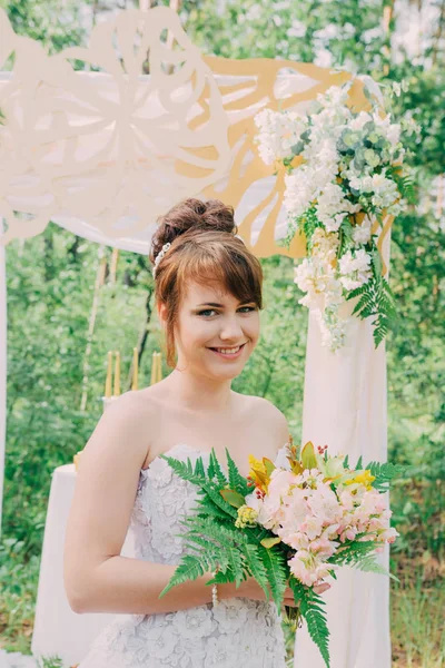 Piękna kobieta w sukni ślubnej na photozone, ozdobione świeżymi kwiatami, pozowanie i portret. — Zdjęcie stockowe