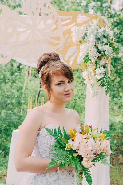 Piękna kobieta w sukni ślubnej na photozone, ozdobione świeżymi kwiatami, pozowanie i portret. — Zdjęcie stockowe