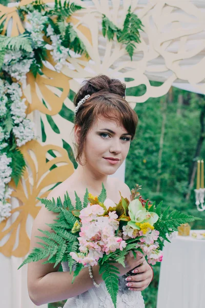 Mooie vrouw in een trouwjurk op een photozone gedecoreerd met verse bloemen, die zich voordeed en portret. — Stockfoto