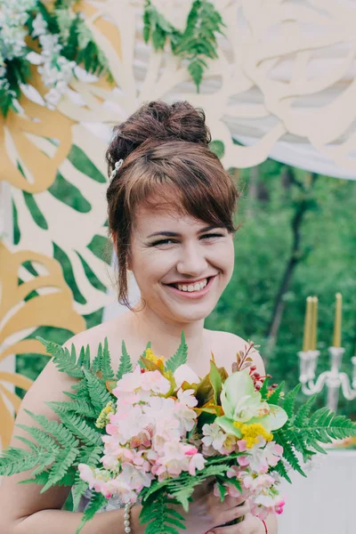 Mulher bonita em um vestido de noiva em uma fotozona decorada com flores frescas, posando e retrato . — Fotografia de Stock