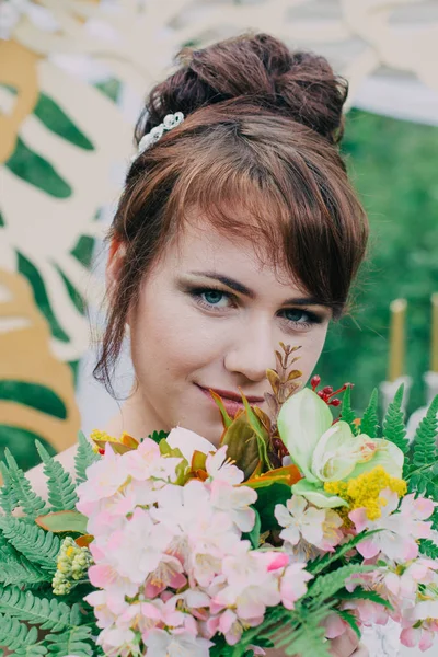 Mooie vrouw in een trouwjurk op een photozone gedecoreerd met verse bloemen, die zich voordeed en portret. — Stockfoto