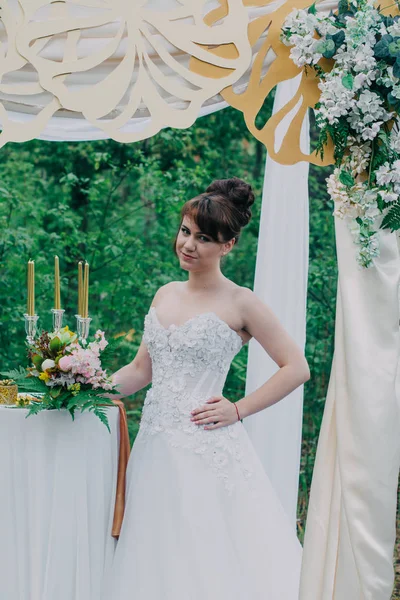 Όμορφη γυναίκα σε ένα γαμήλιο φόρεμα για μια photozone διακοσμημένα με φρέσκα λουλούδια, που παρουσιάζουν και πορτρέτο. — Φωτογραφία Αρχείου