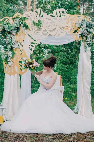 Mooie vrouw in een trouwjurk op een photozone gedecoreerd met verse bloemen, die zich voordeed en portret. — Stockfoto