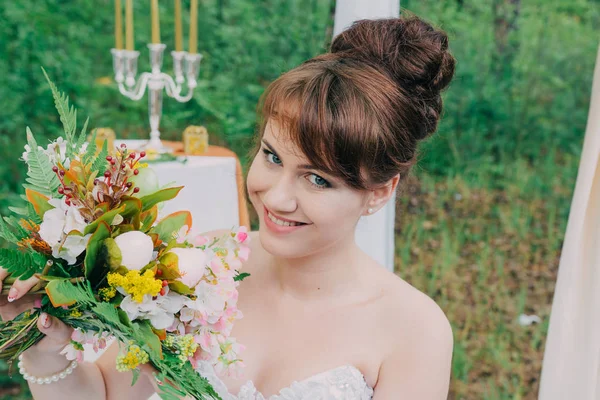 ผู้หญิงสวยในชุดแต่งงาน บนโซนถ่ายรูปที่ตกแต่งด้วยดอกไม้สด โพสและภาพวาด . — ภาพถ่ายสต็อก
