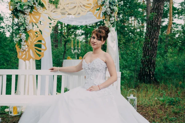 Mulher bonita em um vestido de noiva em uma fotozona decorada com flores frescas, posando e retrato . — Fotografia de Stock