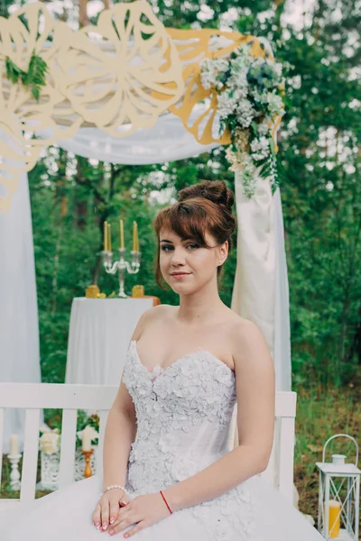 Piękna kobieta w sukni ślubnej na photozone, ozdobione świeżymi kwiatami, pozowanie i portret. — Zdjęcie stockowe
