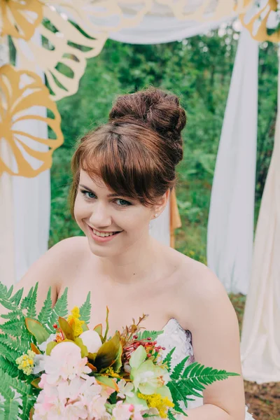 Mooie vrouw in een trouwjurk op een photozone gedecoreerd met verse bloemen, die zich voordeed en portret. — Stockfoto