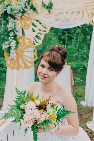 Gyönyörű nő egy esküvői ruha egy photozone azt díszített friss virág, a jelentő és a portré. — Stock Fotó