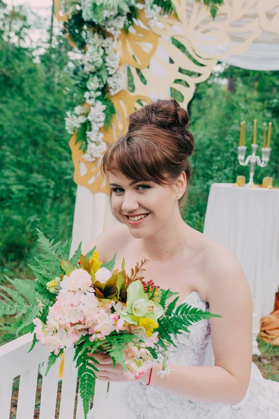 Όμορφη γυναίκα σε ένα γαμήλιο φόρεμα για μια photozone διακοσμημένα με φρέσκα λουλούδια, που παρουσιάζουν και πορτρέτο. — Φωτογραφία Αρχείου