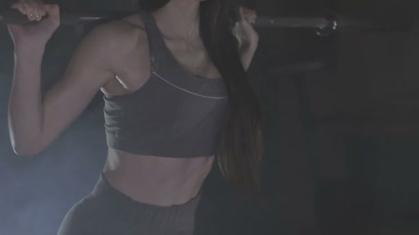 Imagen completa de una mujer joven probando su fuerza sosteniendo una barra con pesas pesadas sobre sus hombros mientras se agacha — Vídeos de Stock