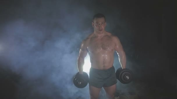 Strong sportsman lifting heavy dumbbells in smoke — Stock Video