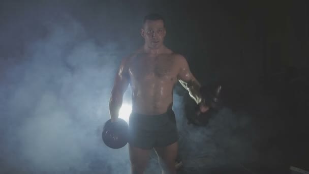 Strong sportsman lifting heavy dumbbells in smoke — Stock Video