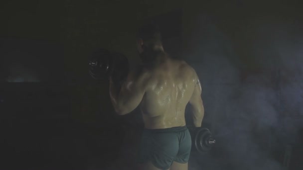Strong sportsman lifting heavy dumbbells in smoke — Stock Video
