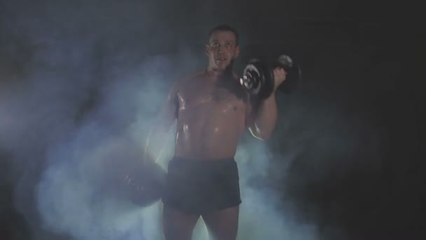 Сильний спортсмен, який піднімає важкі гантелі в диму — стокове відео