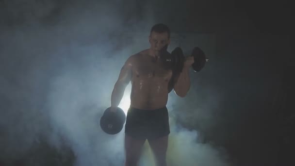 Strong sportsman lifting heavy dumbbells in smoke — Stock Video