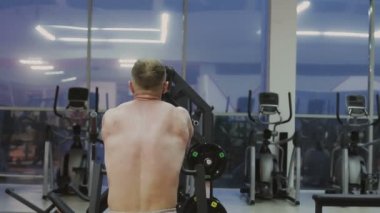 Bir fitness kulübünde fitness makinede kaslı bir adam çıplak bir gövde ile trenler