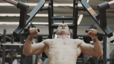 Bir fitness kulübünde fitness makinede kaslı bir adam çıplak bir gövde ile trenler