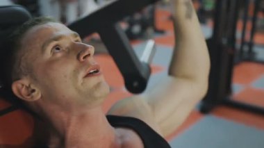 Siyah T-shirt kaslı bir adam bir fitness kulübünde fitness makinede eğitiyor.