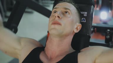 Siyah T-shirt kaslı bir adam bir fitness kulübünde fitness makinede eğitiyor.