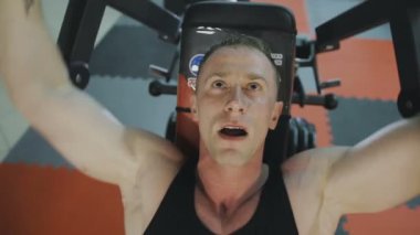 Siyah T-shirt kaslı bir adam bir fitness kulübünde fitness makinede eğitiyor.