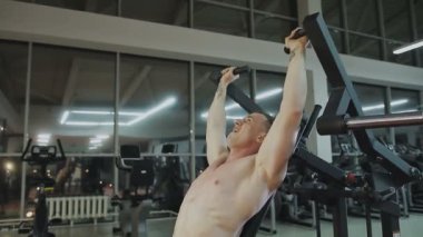 Bir fitness kulübünde fitness makinede kaslı bir adam çıplak bir gövde ile trenler