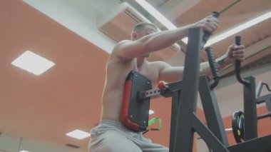 Bir fitness kulübünde fitness makinede kaslı bir adam çıplak bir gövde ile trenler