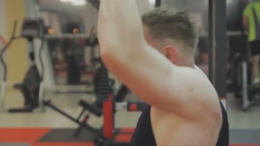 Siyah T-shirt kaslı bir adam bir fitness kulübünde fitness makinede eğitiyor.