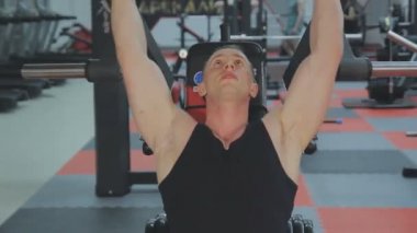 Siyah T-shirt kaslı bir adam bir fitness kulübünde fitness makinede eğitiyor.