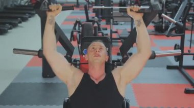Siyah T-shirt kaslı bir adam bir fitness kulübünde fitness makinede eğitiyor.