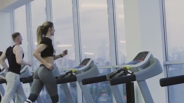 Мужчина и девушка тренируются на беговой дорожке в фитнес-клубе — стоковое видео