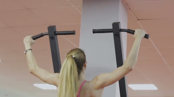 Entrenador de fitness del club deportivo hace pull-ups en el simulador para fortalecer los músculos del hombro. Una mujer hace los ejercicios correctamente, tirando hacia arriba con una espalda recta — Vídeo de stock