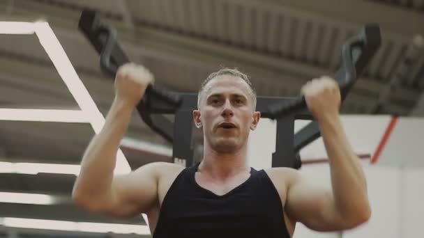 Een gespierde man in een zwart T-shirt is training op een fitnesstoestel in een fitnessclub. — Stockvideo