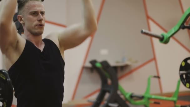 Un hombre musculoso con una camiseta negra está entrenando en una máquina de fitness en un club de fitness . — Vídeos de Stock