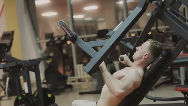 Een gespierde man met een naakte torso treinen op een fitnesstoestel in een fitnessclub — Stockvideo