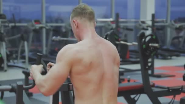 Εκπαιδεύει ένα μυϊκό άνθρωπο με γυμνό τον κορμό σε μια μηχανή φυσικής κατάστασης στο γυμναστήριο — Αρχείο Βίντεο