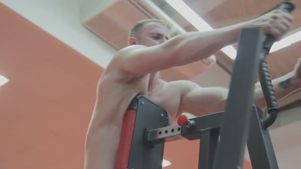 Un hombre musculoso con un torso desnudo entrena en una máquina de fitness en un club de fitness — Vídeo de stock