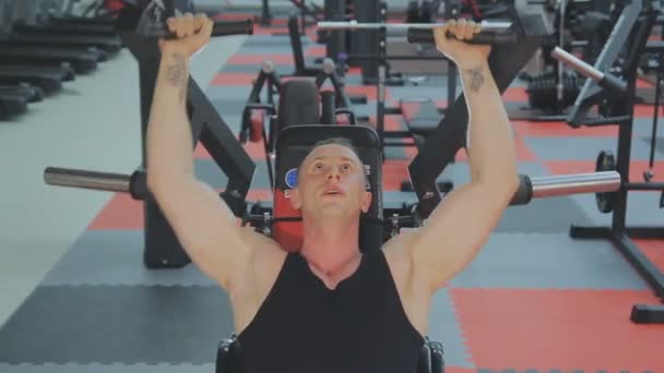 М'язистий чоловік у чорній футболці тренується на фітнес-автоматі у фітнес-клубі . — стокове відео