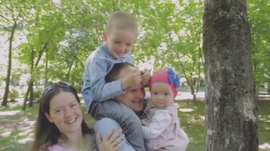 Aile ile çocuk parkta yürüyor. Güneşli bir gün. Yeşil ağaçlar